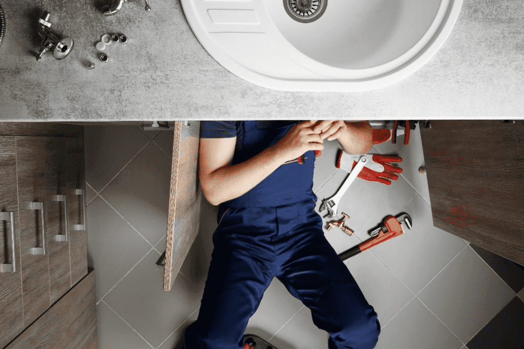 Male plumber repairing sink pipes in kitchen