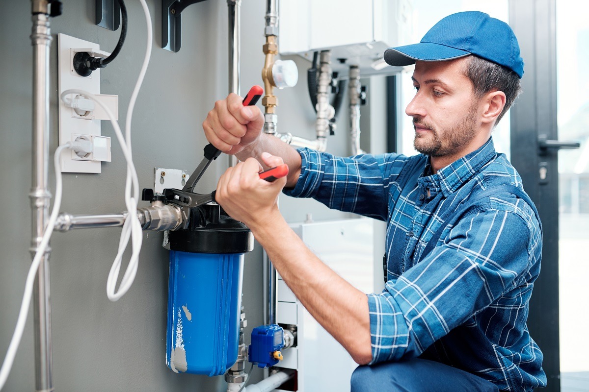 Young plumber installing or repairing system of water filtration