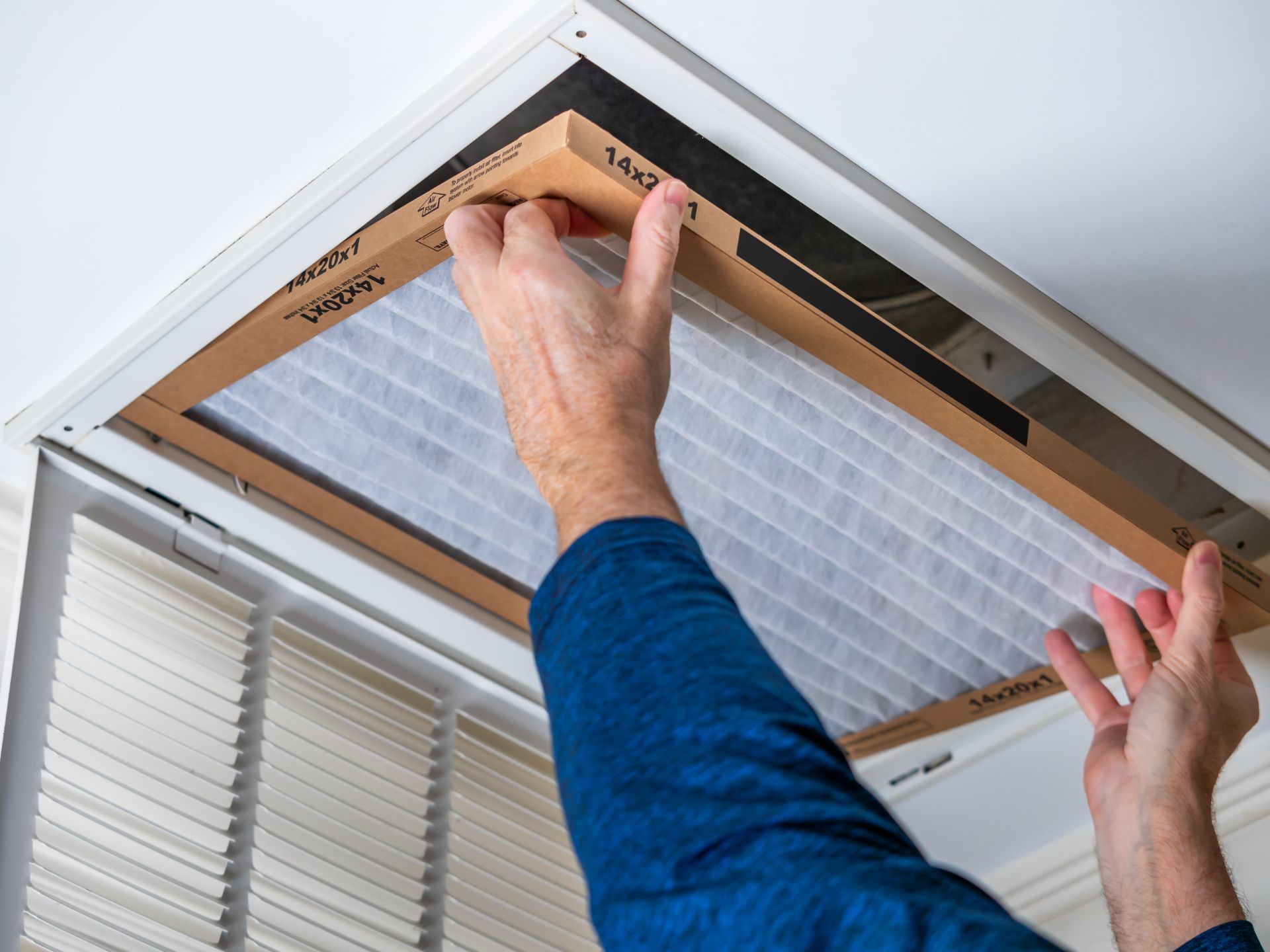 Man replacing dirty HVAC air filter in ceiling vent.